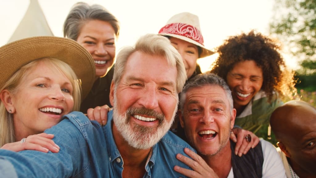 Close Up Portrait Of Mature Friends Posing For Selfie Outdoors Against Flaring Sun